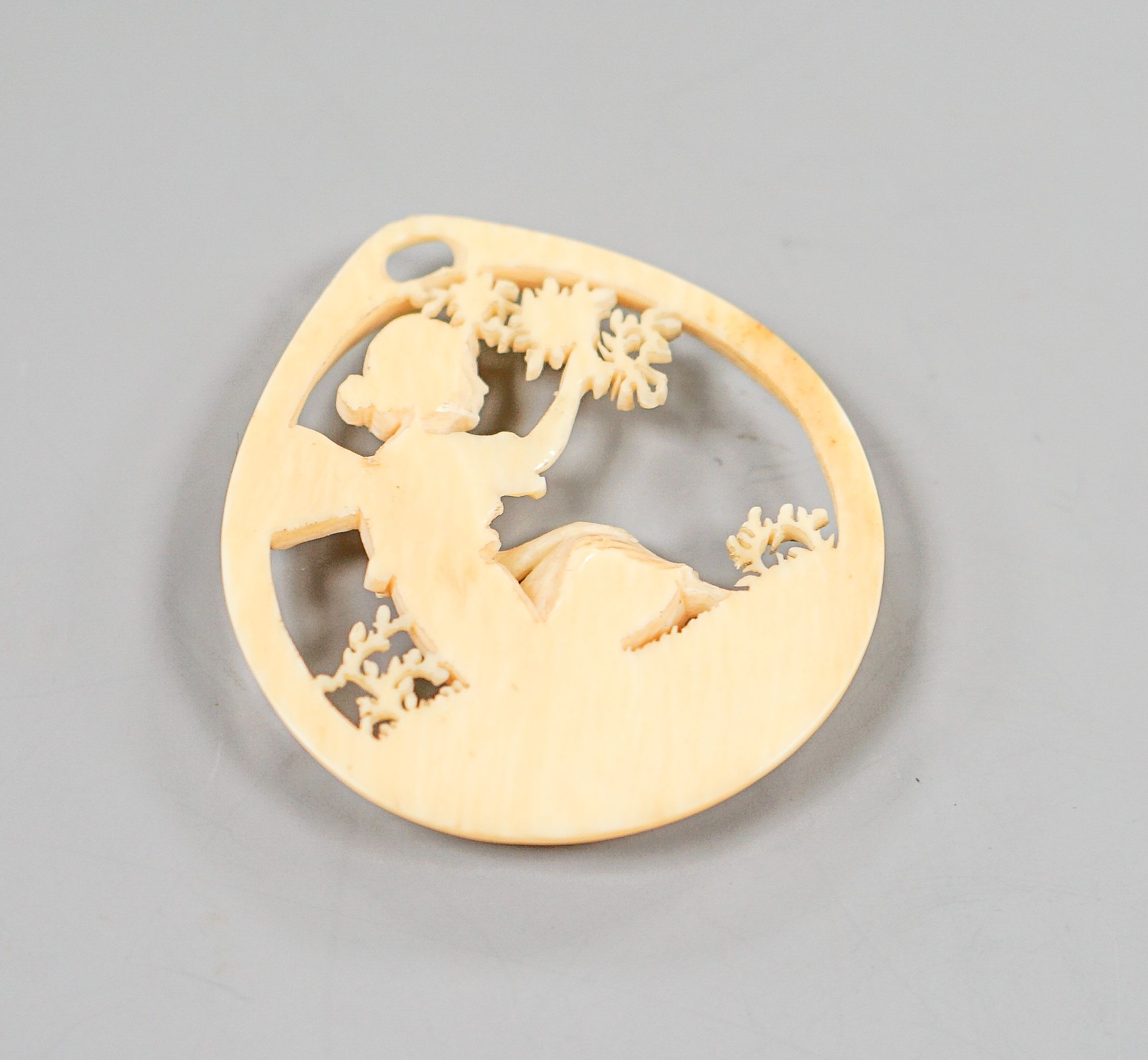 A carved ivory pendant, modelled as a seated fairy, 50mm.